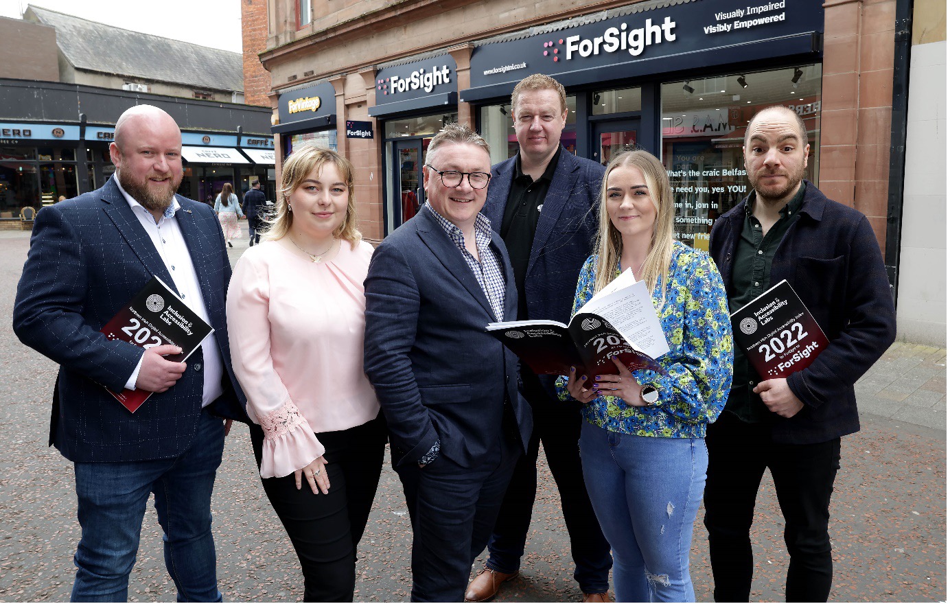 Sean Doran, Adela Buliman, Chris White, Kyran O'Mahoney, Amanda McClure, and Robbie Best holding the NI DAI Report in front of a ForSight shop.